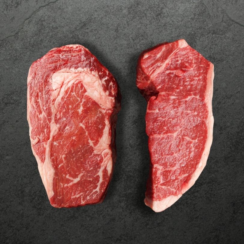 overhead view of a raw canadian prime ribeye steak and New York strip steak