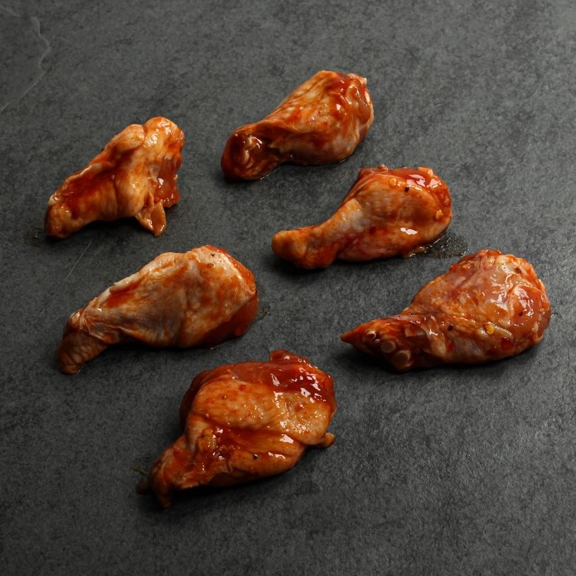 angled view of six raw, spicy bbq-marinated chicken drumettes