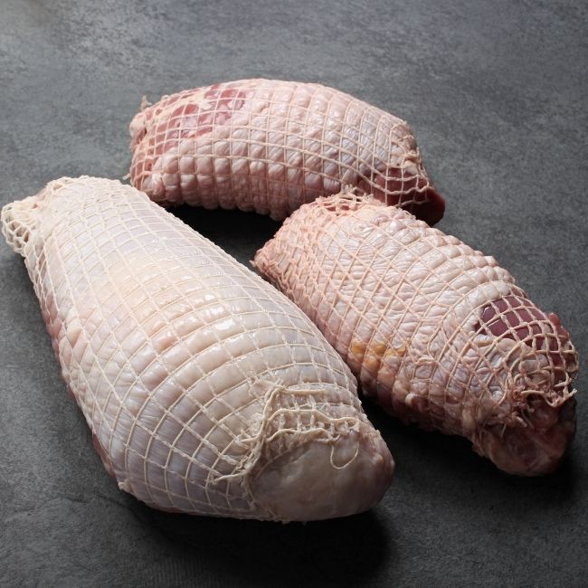 angled view of a raw netted turkey breast and two raw netted turkey thighs