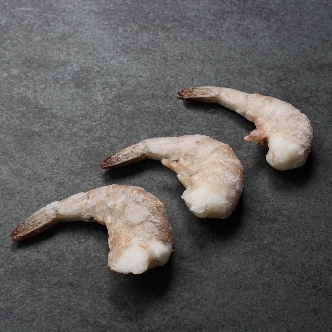 angled view of three raw, frozen jumbo shrimp
