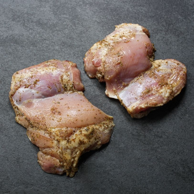angled image of 2 raw, boneless, skinless chicken thighs lightly coated in a greek marinade