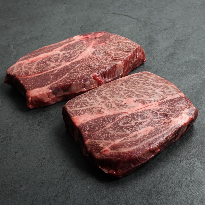 angled view of two raw, heavily marbled chuck eye steaks