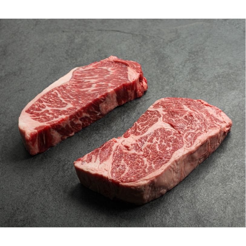 angled view of a raw New York steak and ribeye steak