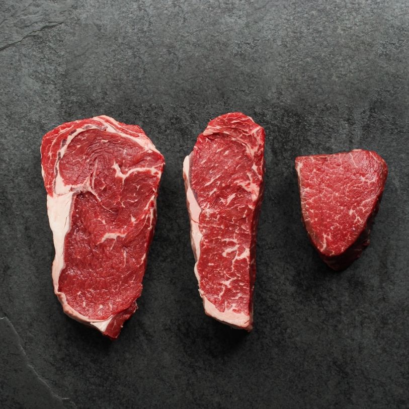overhead view of a raw rib eye steak, raw new york steak and raw filet mignon