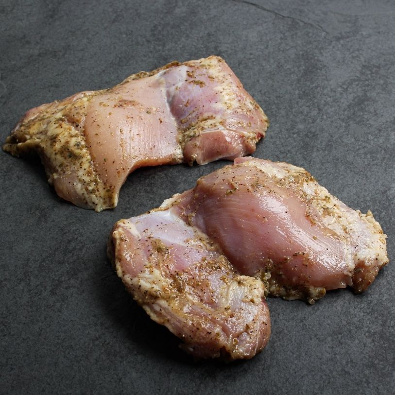 angled image of 2 raw, boneless, skinless chicken thighs lightly coated in a greek marinade