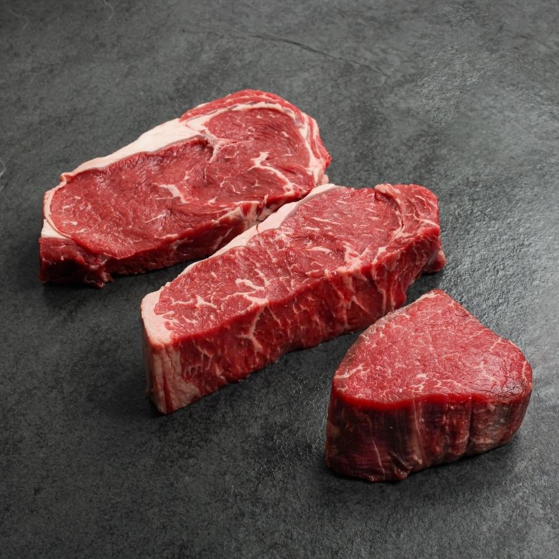angled view of a raw rib eye steak, raw new york steak and raw filet mignon