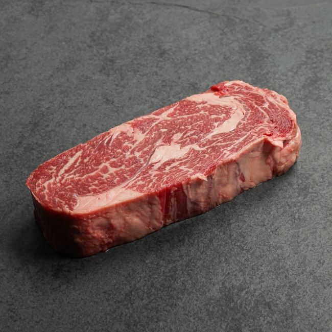 angled view of a raw, well-marbled grass fed ribeye steak